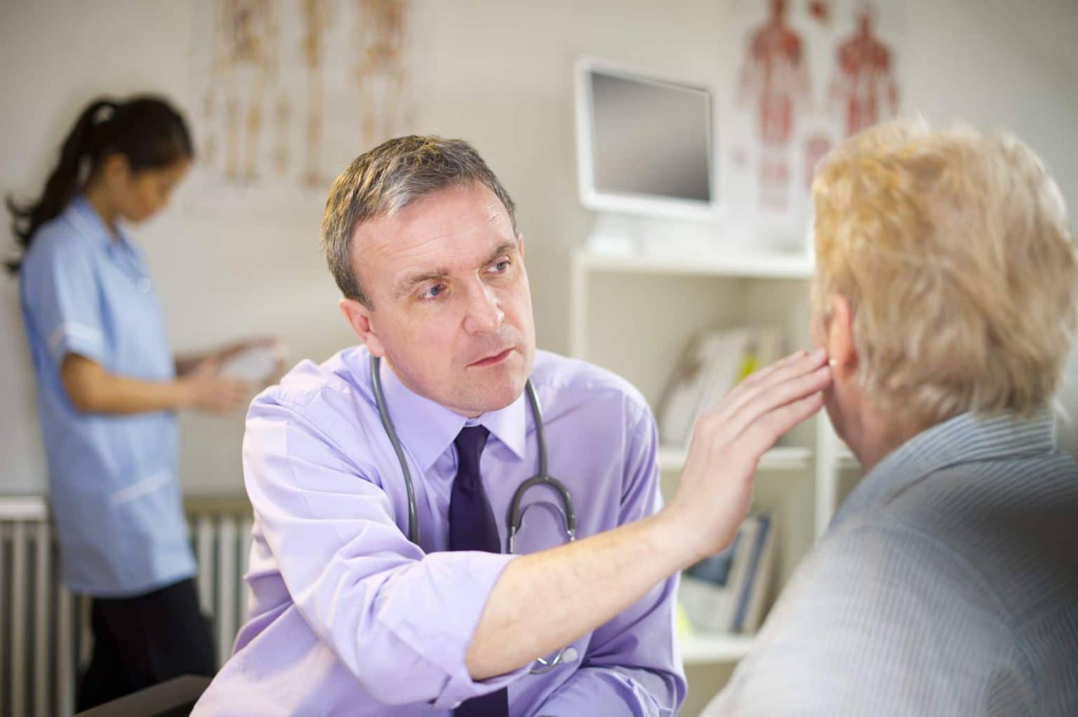 ENT is holding his hand against a patients ear as he discusses symptoms related to earwax pain that may require removal.