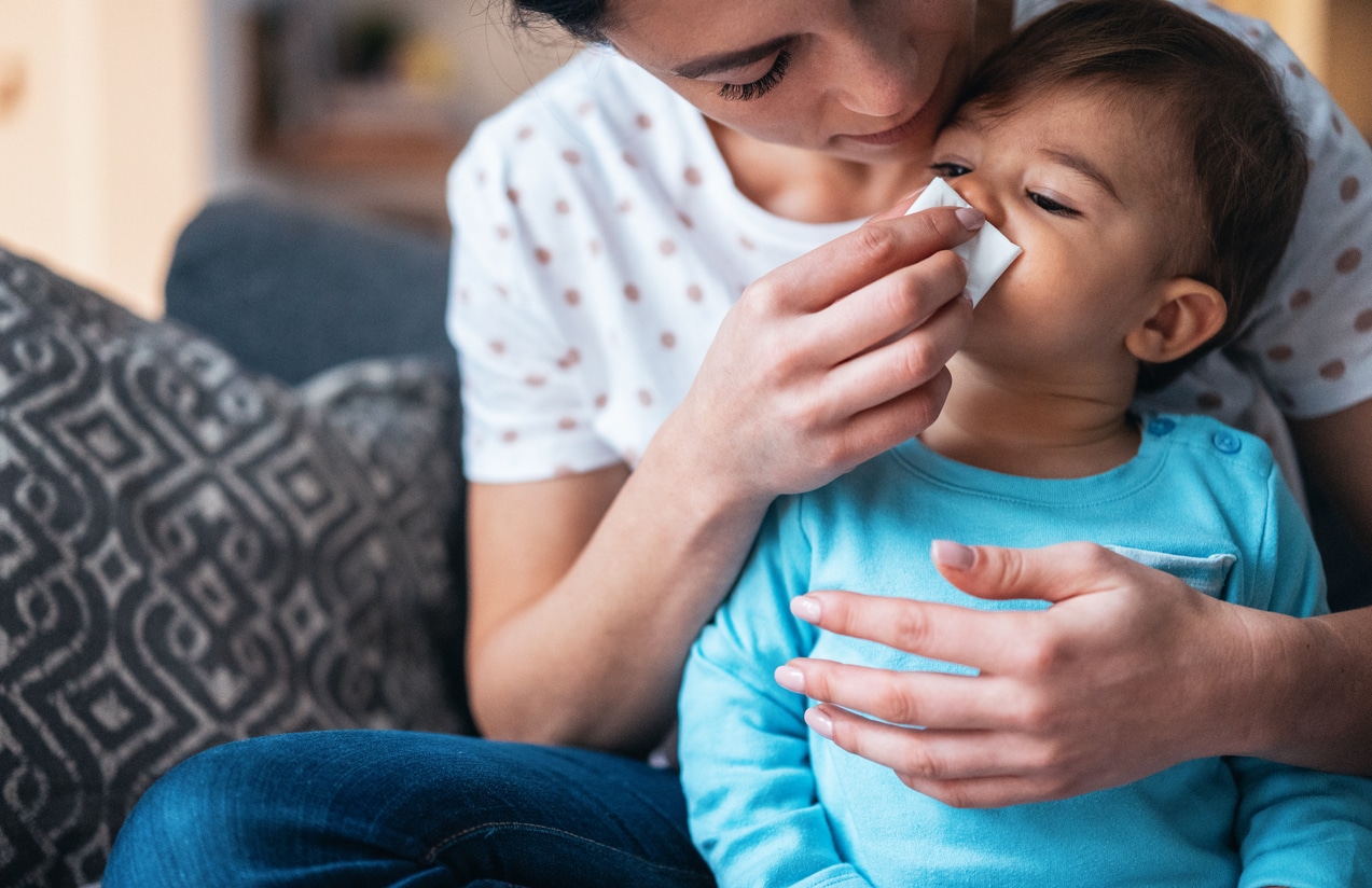 Mother helping her infant son blow his nose