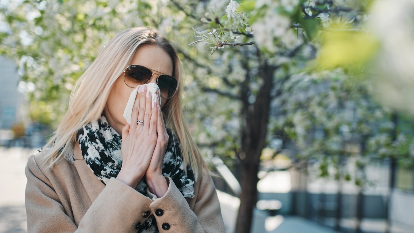 Woman blowing her nose near some trees